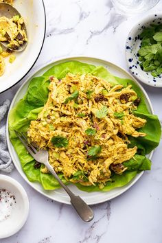 a white plate topped with lettuce covered in chicken next to bowls of food