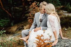 a bride and groom are sitting on a rock in the woods looking at each other