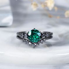 a ring with a green stone in the center on a white plate next to flowers