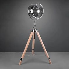 an old fashioned fan sitting on top of a wooden tripod next to a gray wall