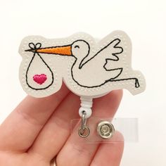 a white stork badge with a pink heart on it