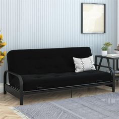 a black futon sofa sitting on top of a wooden floor next to a table