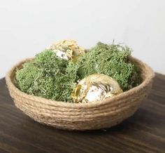 a basket filled with moss covered eggs on top of a wooden table