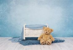 a brown teddy bear sitting on top of a blue rug next to a white bed