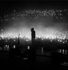 a man standing on top of a stage with lots of lights in the sky behind him