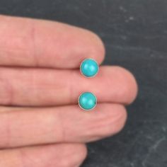 A pair of turquoise post earrings made with 6mm cabochons. Blue with a hint of green. Set in fine silver bezels and soldered onto sterling silver posts. They've been given a satin finish leaving a frame of bright silver visible around the turquoise. Sterling ear nuts included (7mm including setting -- see the picture on the model for size reference). Available in bright satin or oxidized finish (4th picture) DETAILS Stones: Natural Turquoise, stabilized to protect their color, not enhanced. Meta Turquoise Round Birthstone Earrings, Turquoise Birthstone Round Earrings, Natural Turquoise, Earrings Sterling Silver, Turquoise Earrings, Silver Studs, Fine Silver, Post Earrings, Turquoise Ring