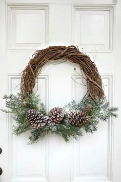 a wreath with pine cones and greenery is hanging on the front door