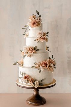 a white wedding cake with pink flowers on top and greenery around the edges, sitting on a wooden stand