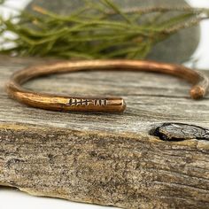 a close up of a wooden surface with a metal bracelet on it and a plant in the background