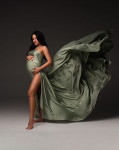 a pregnant woman in a green dress posing for a photo with her long flowing fabric