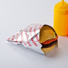 a sandwich wrapped in aluminum foil next to an orange shaker and yellow plastic bottle