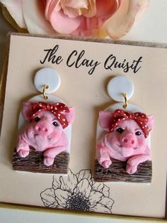 a pair of pink pig earrings sitting on top of a card next to a flower