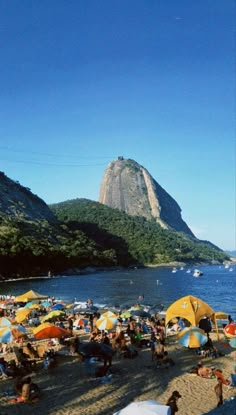 many people are on the beach with their umbrellas up and there is a mountain in the background