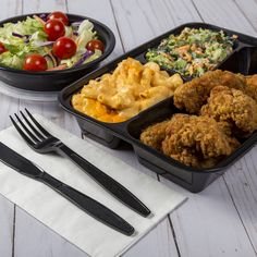 two black plastic containers filled with food next to a fork and knife on top of a white table