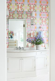 the bathroom is decorated with colorful wallpaper and white cabinets, along with a large mirror