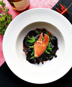 a white bowl filled with food on top of a pink table cloth next to a bottle of wine