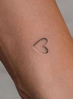 a woman's arm with a small heart tattoo on the left side of her arm