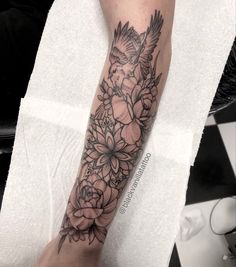 a woman's arm with flowers and a bird tattoo on her left forearm,