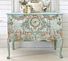 an ornate painted dresser in front of a white wall with a mirror and vases on top