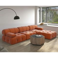 an orange couch sitting in front of a window next to a wooden table with a lamp on it