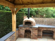 an outdoor brick pizza oven in the middle of a patio with wood and stone walls