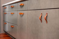 an orange handle on a gray cabinet with wood flooring and walls in the background