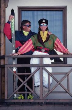 two people standing on a balcony with skis in their hands and one person wearing sunglasses