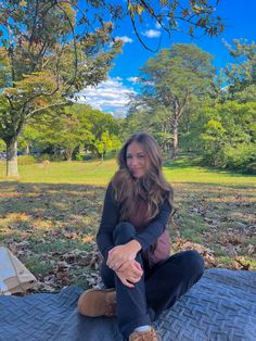 a woman sitting on top of a blanket in the park