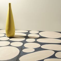 a yellow vase sitting on top of a table next to a black and white floor