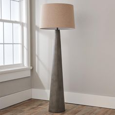 a lamp that is on top of a wooden floor next to a white wall and window