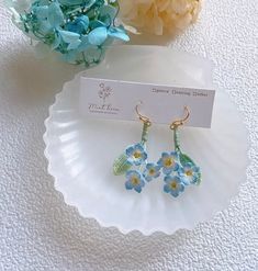 two small blue flowers are sitting on a plate next to a flower vase and a business card