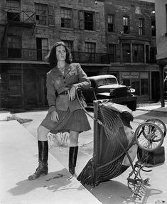 a woman in an old fashion dress and boots standing next to her stroller on the sidewalk