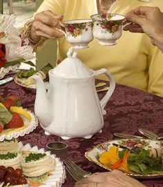 an older woman pouring tea into two cups at a table with other plates and dishes on it