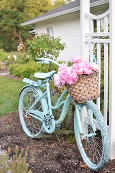 a blue bicycle with pink flowers in the basket parked next to a white picket fence