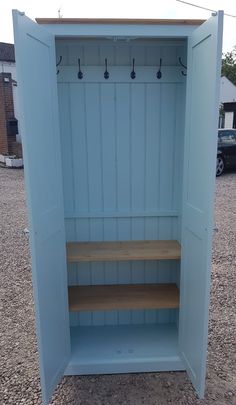 an empty blue storage cabinet with wooden shelves and hooks on the door, sitting in gravel