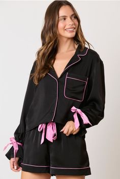 Lounge in style with our Black Satin Bow Detail Pajamas. The set features a sleek black design with pink satin bow and piping details. The v-neck style and long sleeves add a touch of elegance, while the front pocket and pull on elastic waist shorts provide comfort and convenience. Feel effortlessly chic in this must-have pajama set. Qualifies for Free Shipping. Details: 2 piece set Bow detail V-neck Collared Front pocket Button front closure Elastic waist shorts Fits TTS Imported Model Specs: A Black Satin Loungewear Sets, Black Satin Long Sleeve Sleepwear, Shorts Fits, Game Dresses, Elastic Waist Shorts, Satin Bow, Comfy Cozy, Short Sleeved Sweaters, Pink Satin