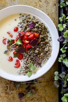 a white bowl filled with soup and vegetables on top of a table next to flowers