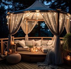 an outdoor gazebo with lights and pillows on the floor, surrounded by greenery