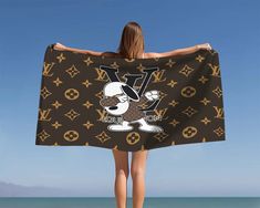 a woman is standing on the beach with her back to the camera, holding up a louis vuitton towel