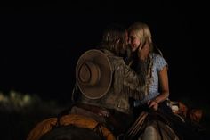 two people riding on the back of a brown horse in the dark with their arms around each other