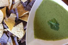 a white bowl filled with green liquid surrounded by tortilla chips