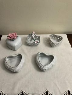 four white ceramic heart shaped dishes on a table with a lace doily around the edges