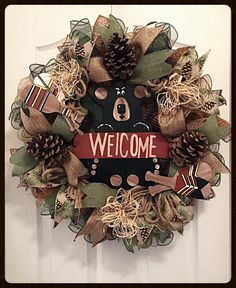 a wreath with the word welcome hanging on it's front door decorated with pine cones and ribbons