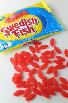 red candy candies are next to a bag of swedish fish gummies on a white table