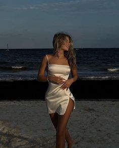 a woman standing on top of a sandy beach next to the ocean wearing a white dress