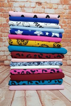 a stack of different colored fabrics sitting on top of a wooden table next to a brick wall