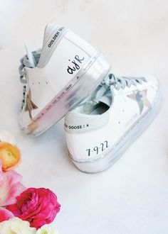 a pair of white tennis shoes sitting on top of a table next to pink flowers