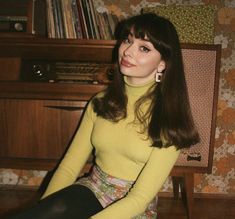 a woman sitting on the floor in front of a piano wearing a yellow sweater and floral print skirt