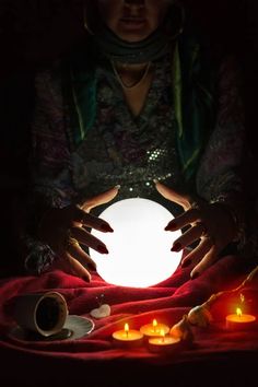 a woman is holding out her hands over a glowing orb in the dark with candles around it