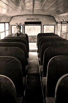 a man with a goat mask sitting in the back of an empty bus, looking out the window